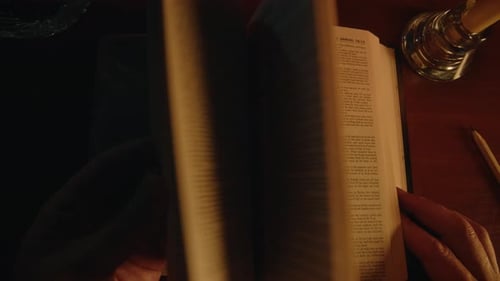 Hands Turning Pages of Open Book at Night