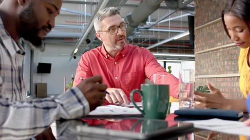 Diverse colleagues sitting at table in discussion at meeting in casual office, slow motion
