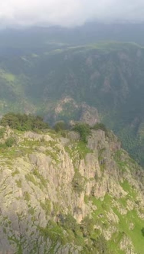 Luftbilddrohne von Rocky Cliff und Green Hills, die um ein vertikales Video fliegt