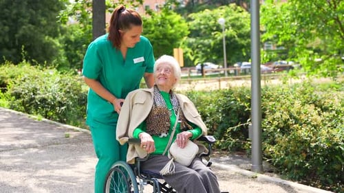 An elderly woman with the nurse on a walk in the garden of a nursing home in a wheelchair next to na