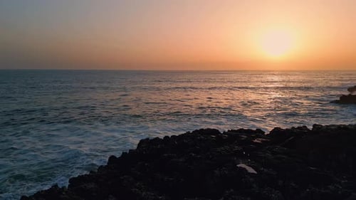 Dramatic ocean surf rolling along a rocky cliff coastline at sunrise