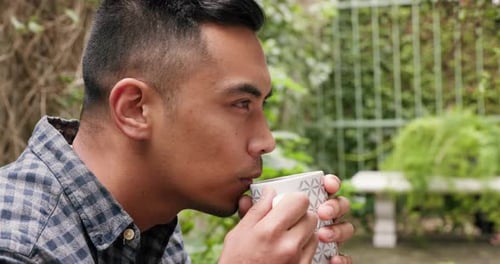 Thinking, serious and man drinking coffee while sitting in a backyard garden alone outdoor