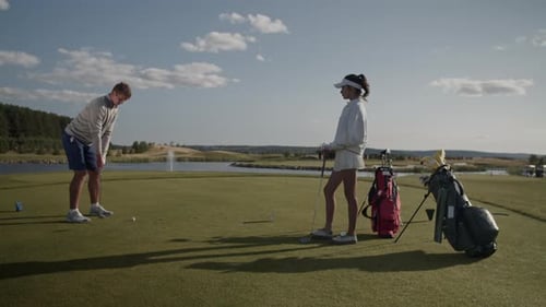 Young Man Swings Golf Club to Hit Ball As Woman Stands Nearby