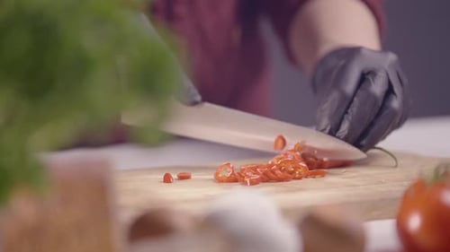 Zeitlupen-Nahaufnahme eines Küchenchefs, der rote Chili-Pfeffer präzise in Scheiben schneidet
