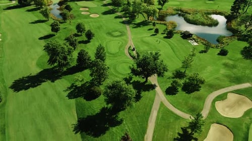 Aerial drone tilt up shot of green golf club covering large area along with small pond on a sunny da