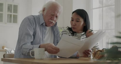Senior Man and Caring Young Woman Counting Taxes and Paying Bills Talking in Kitchen in Apartment