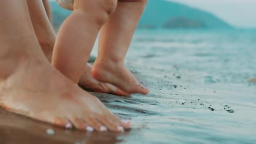 Mother And Baby Feet Standing On Beach. Mom Helping Baby Stand And Walk On Sea Beach. Mother And ...