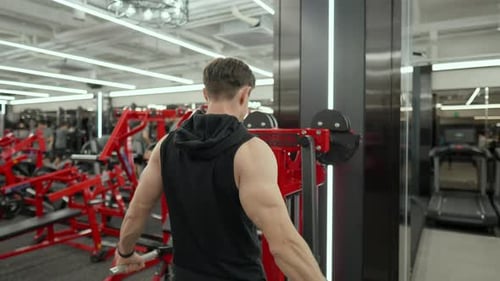 Mascular Adult Male Perform Shoulder Side Raise Exercise in Machine at Fitness Center - rear view