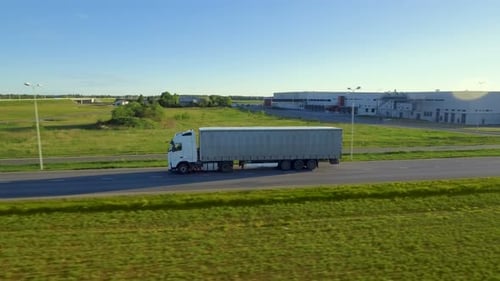 Aerial Side View of White Semi Truck with Cargo Trailer Moving on the Highway. In the Background W
