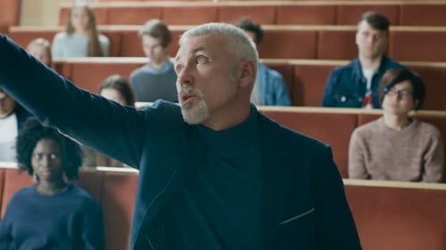 Clase frente a la cámara: un profesor destacado escribe en la pizarra y lee una conferencia a una clase o