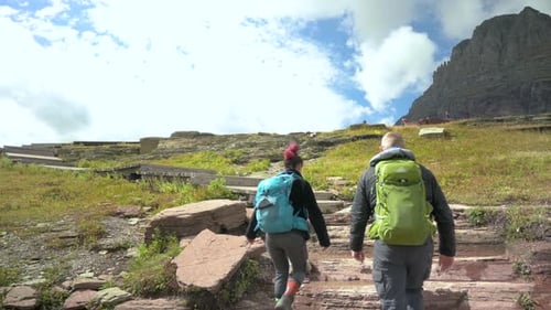 Hikers climbing stone stairs on Hidden Lake Trail in Glacier National Park with Mount Clements in th