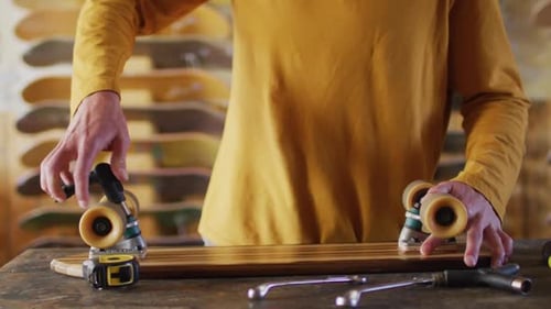 Video of midsection of caucasian male skateboarder fixing skateboard in skate shop