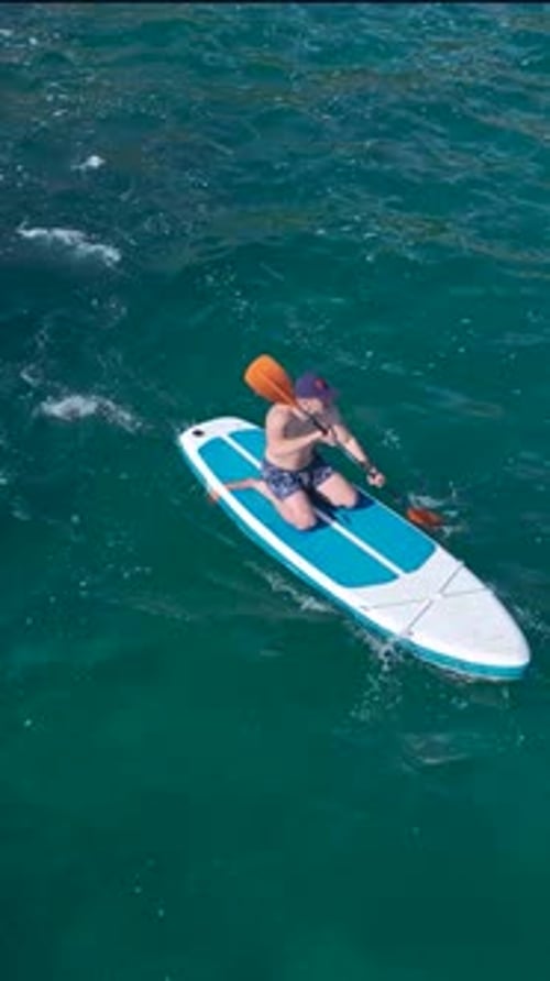Vertical Video SUP Riders Paddle Gently in the Open Sea Relaxing on Boards Over Clear Azure Waters