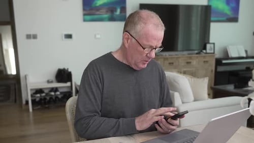 Man Uses Laptop and Phone Indoors at Home