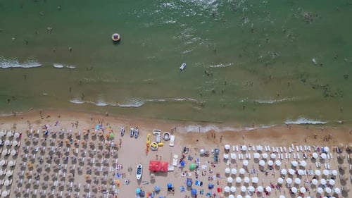 Drone Video of a Crowded Beach with Rows of Umbrellas and Sunbathers Set Against the Gentle Waves of