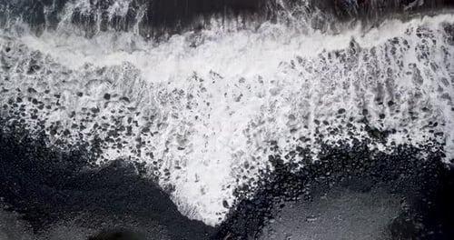 Foamy and powerful waves splash on the black-sand beach of Maui, Hawaii. Aerial top-down view, cinem