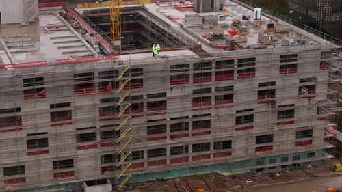 Toma aérea de técnicos de una obra de construcción con chaquetas reflectantes discutiendo sobre la parte superior de la estructura