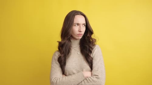 Annoyed Woman with Arms Crossed on Yellow Background