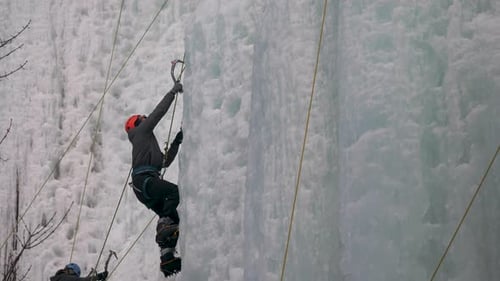 Man uses ice picks to climb upwards on a wall of ice