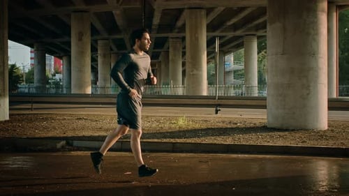 Athletic Young Man in Sports Outfit is Jogging in the Street. He is Running in an Urban Environment