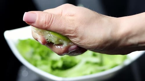 Splash of lime juice close up in slow motion. Hand squeezing half of a fresh lime