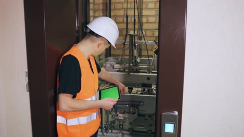 Mit einem digitalen Tablet reguliert der Ingenieur das Sicherheitssystem des Aufzugs. Ein Reparaturingenieur ist