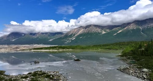 Rising over the river reflecting the beautiful mountains covered with fluffy clouds at the tops.