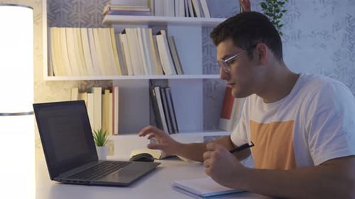 Young Adult Working at Desk with Laptop and Notebook