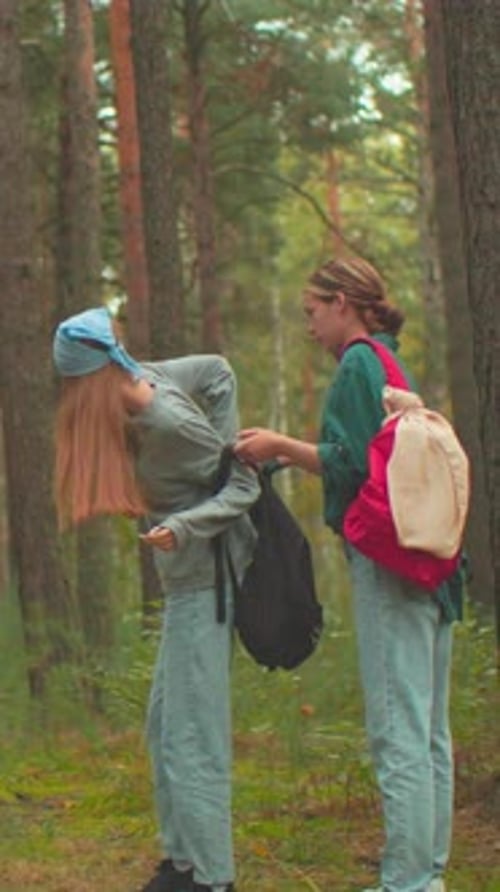 Two Women Prepare for Hike in Peaceful Forest Assisting Each Other with Backpacks