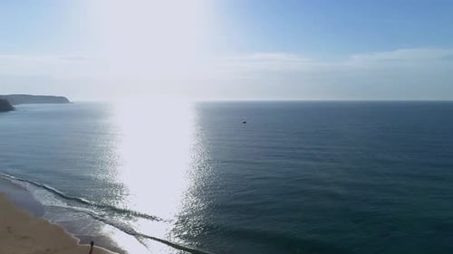 Aerial tilting view of people walking at beautiful beach while waves crashing at sunrise