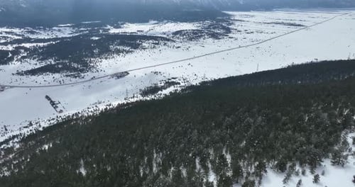 Aerial Drone Shot Over Leafless Trees Above a Snowy Mountain and Beautiful Snowy Mountain Peaks