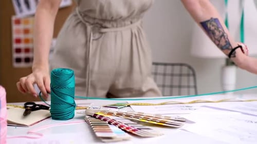 Smiling Tailor Measures Green Thread with Tape on Table in Fashion Studio Woman Designer Work