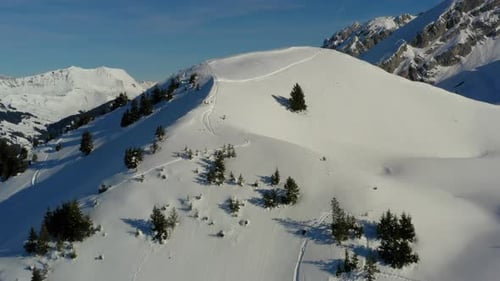 Aerial view rising up above a snow covered mountain peak to reveal a mountain valley and ski resort