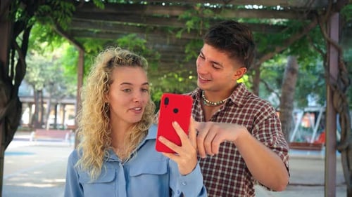 Smiling Young Couple Using Phone in Green Park