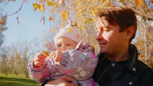 A Heartwarming Moment Between a Father and His Baby in Autumn with Colorful Leaves in the Background
