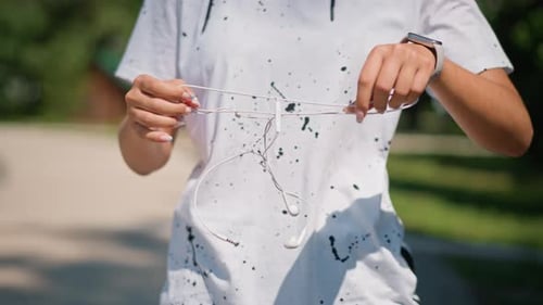 Musician Fixing Earbuds Musician Carefully Sorts Tangled Earbuds on Park Pathway Calm Artist