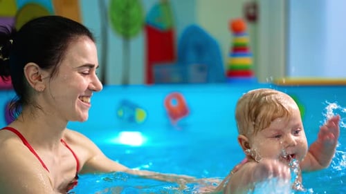 Smiling female coach holding a baby in the swimming pool.