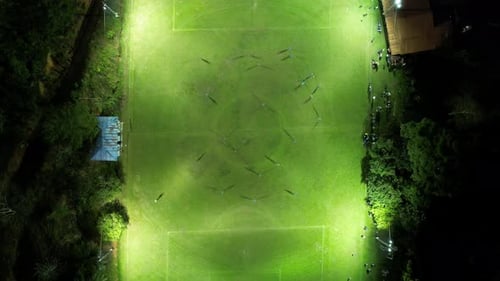 Aerial top down of two sport teams playing soccer at night in an illuminated grass field. Timelapse.
