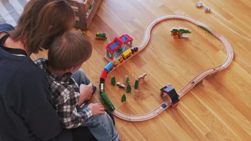 Child and Adult Playing with Toy Train at Home