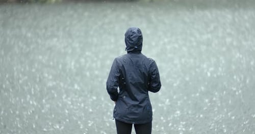 Woman Stands in the Pouring Rain Against the Background of a Lake Shot on Super Slow Motion Camera