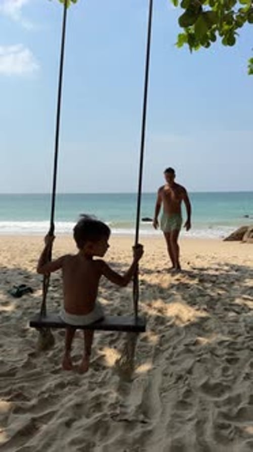 Father Pushing Son on Swing at the Beautiful Beach