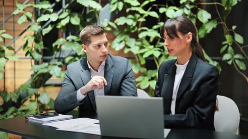 Business Colleagues in Office Discuss Project Strategy Using Laptop and Documents