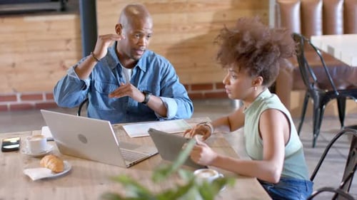 Collègues afro-américains, homme penché, faisant des gestes, mentorant, femme tenant une tablette, un stylet sur un ordinateur portable