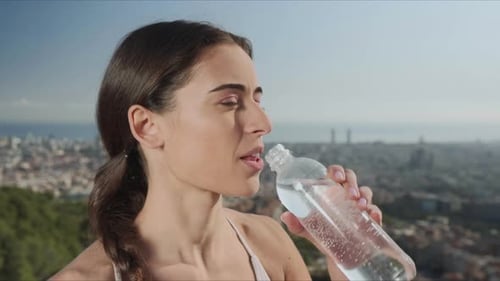 Happy Woman Opening Bottle with Water at City View. Athletic Girl Drinking