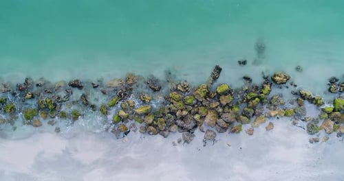 Splashing Blue Ocean Water Among Rocks Covered in Algae Along the Seashore Aerial Crane