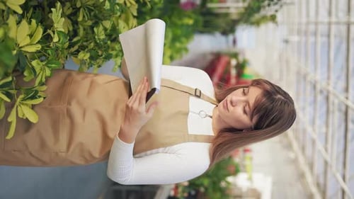 Une fleuriste debout travaillant dans une serre inspectant des plantes