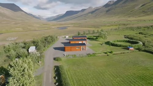 Drone footage flies over a village with a green landscape and a river in Iceland