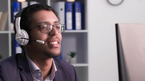Afro American Man in Glasses Talking to a Client Via Video Call Using a Microphone on Headphones