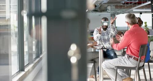 African american businessman wearing vr headset, gesturing while colleagues watching him at office
