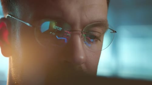 Trader Wearing Glasses is Working on Laptop Computer Screen with Stock Market Charts and Bitcoin BTC
